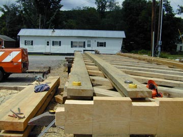 A completed truss stands by the trailer-born salvaged roof.